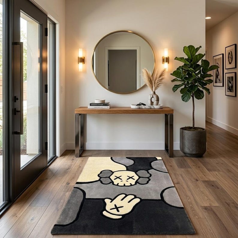 K&ouml;nnte beinhalten: Ein rechteckiger Teppich mit einem stilisierten Grafikdesign in einer Farbpalette aus Creme, Grau und Schwarz. Das Muster zeigt ein zentrales Totenkopfmotiv mit X-f&ouml;rmigen Augen und ein Handsymbol mit einem X auf der Handfl&auml;che in kr&auml;ftigen Linien.