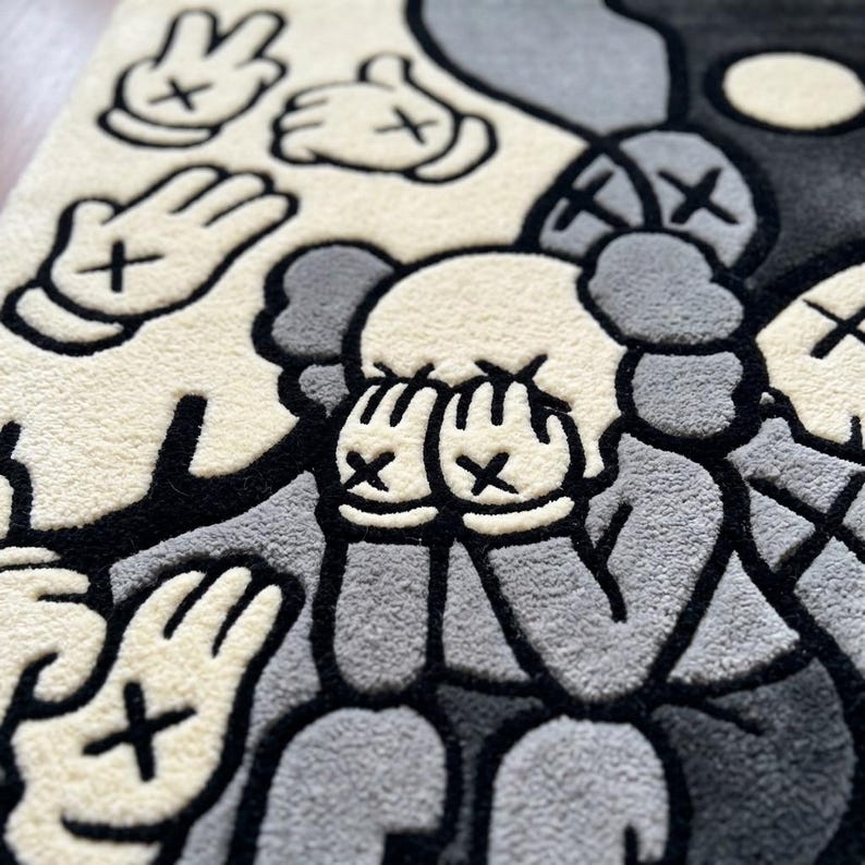 May include: A tufted rug featuring a graphic illustration in shades of cream, gray, and black. The design depicts a character with hands covering its face, surrounded by multiple floating hands, all characterized by X-shaped eyes and thick black outlines.