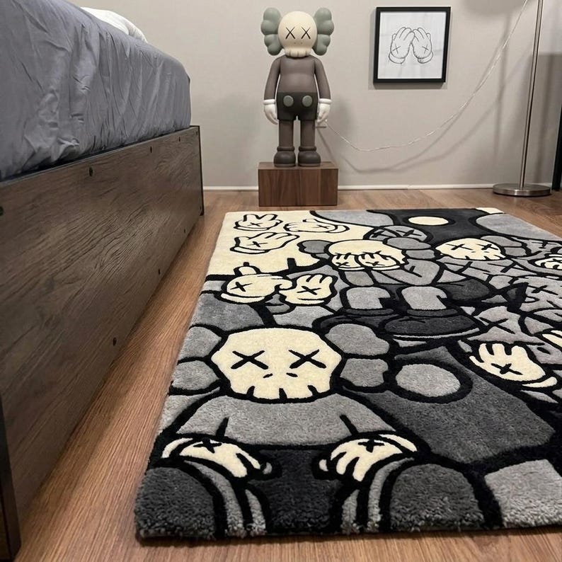 May include: A rectangular area rug featuring a repeating pattern of cartoon-style characters with skull-like heads and gloved hands. The design uses a monochromatic color palette of black, white, and various shades of gray with thick black outlines.