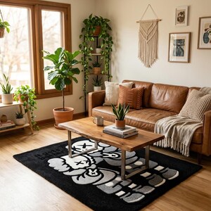 K&ouml;nnte beinhalten: Ein rechteckiger schwarzer Teppich mit einer gro&szlig;en, stilisierten grau-wei&szlig;en Cartoon-Figur und dem Text "It gets better" in der Ecke. Der Teppich liegt auf einem hellen Holzboden unter einem Couchtisch aus Holz.
