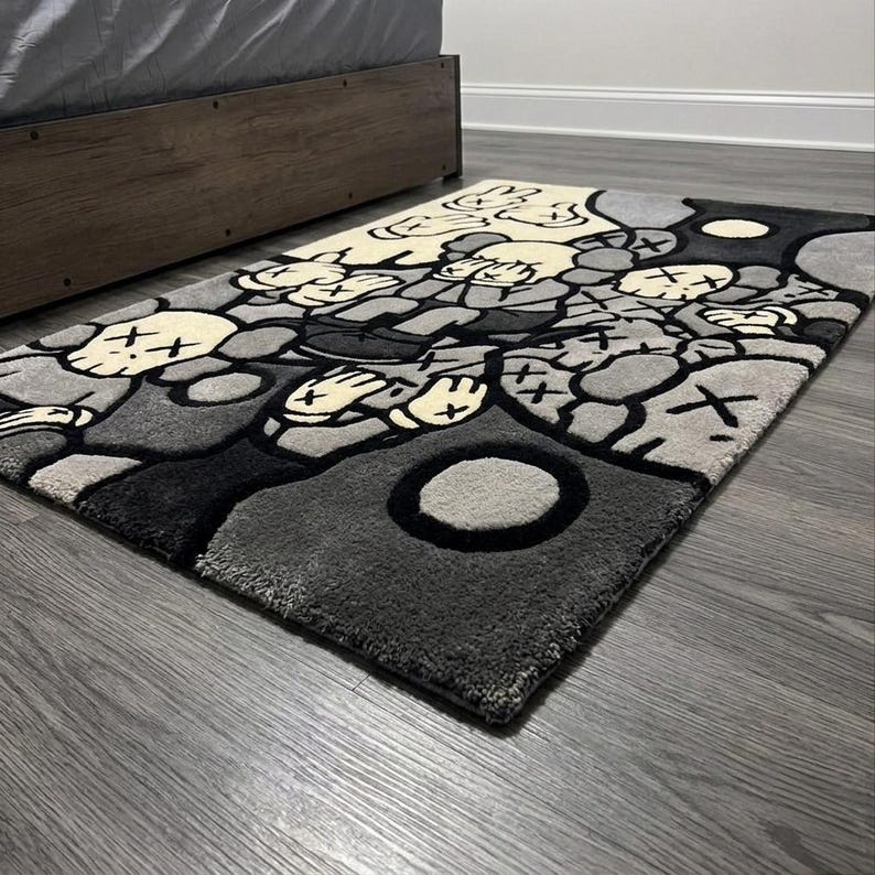 May include: A rectangular area rug featuring a repeating graphic pattern of cartoon-style characters with X-shaped eyes and gloved hands. The design uses a monochromatic color palette of black, dark gray, light gray, and cream, with bold outlines.