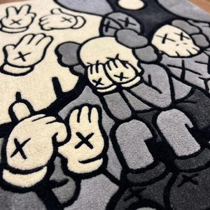 May include: A tufted rug featuring a monochromatic graphic design in shades of cream, gray, and black. The pattern displays multiple cartoon-style gloved hands with X-shaped markings on the palms and figures with X-shaped eyes covering their faces.