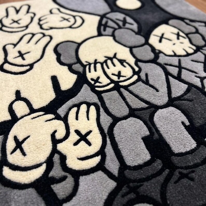 May include: A tufted rug featuring a monochromatic graphic design in shades of cream, gray, and black. The pattern displays multiple cartoon-style gloved hands with X-shaped markings on the palms and figures with X-shaped eyes covering their faces.