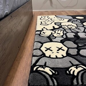 May include: A rectangular area rug featuring a repeating graphic pattern of cartoon-style characters with X-shaped eyes and gloved hands. The design is rendered in a palette of black, white, and various shades of gray with thick black outlines.