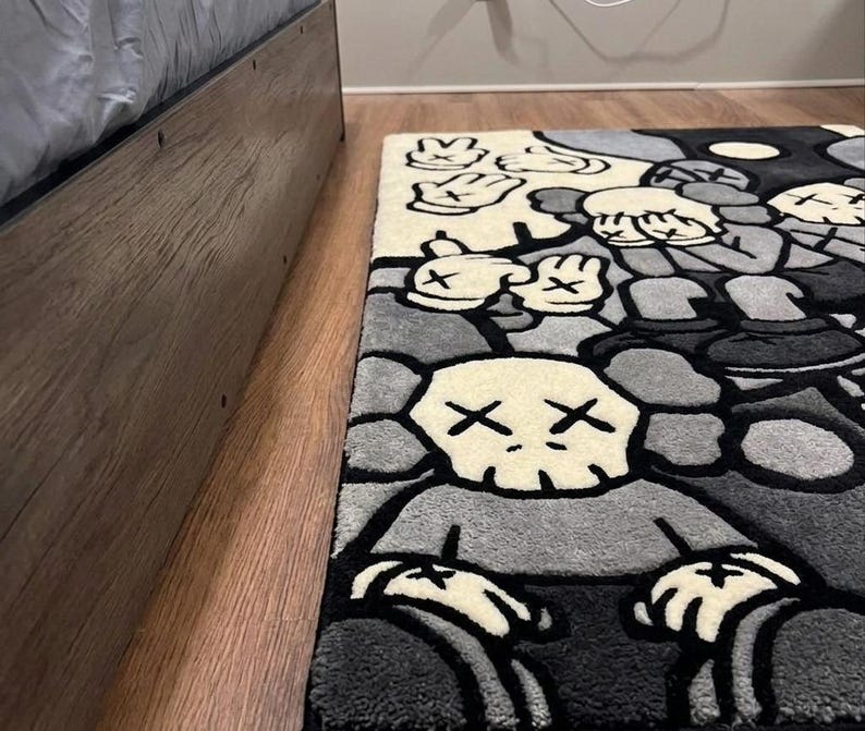 May include: A rectangular area rug featuring a repeating graphic pattern of cartoon-style characters with X-shaped eyes and gloved hands. The design is rendered in a palette of black, white, and various shades of gray with thick black outlines.