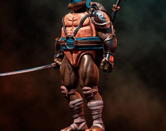 Puede incluir: Figura de acción detallada de Leonardo de las Tortugas Ninja. La figura es marrón y beige con una máscara azul, armadura y una katana. Se encuentra sobre una base de piedra y posa con una espada.
