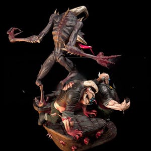 May include: A detailed, multi-figure sculpture of a monstrous creature with horns, spikes, and a long tongue, towering over two figures. The figures are in a dark color palette with red accents, set against a black background.