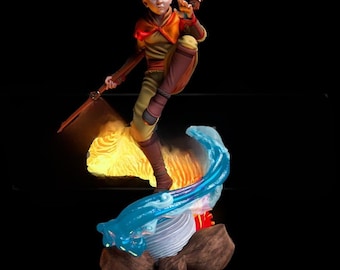 May include: A detailed figurine of a character in a dynamic pose, with a bald head and blue eyes, wearing yellow and orange attire. The figure is surrounded by stylized fire and water elements, with a staff in hand. The base features rock-like formations.