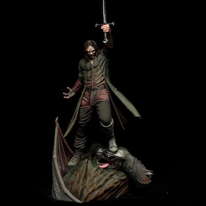 Può includere: Statuetta dettagliata di un guerriero con un lungo cappotto verde, che tiene una spada in alto. La figura è in piedi su una creatura simile a un drago con la lingua di fuori. Il guerriero indossa abiti marroni e neri.