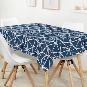 Puede incluir: Un mantel azul marino con un patrón geométrico blanco cubre una mesa. El mantel está sobre una mesa con sillas blancas y patas de madera clara. El diseño geométrico consiste en líneas blancas que forman formas irregulares. La mesa mide aproximadamente 150 cm de largo.
