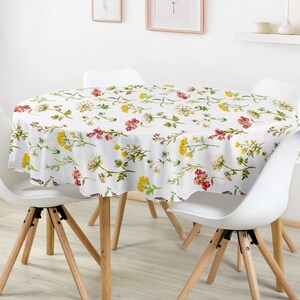 Peut inclure: Une nappe ronde blanche ornée d'un motif floral avec des fleurs jaunes, rouges et roses. La nappe recouvre une table ronde, entourée de quatre chaises blanches avec des pieds en bois. La pièce a un design minimaliste.