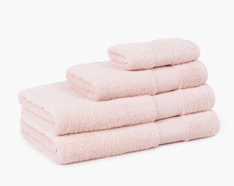 Può includere: Una pila di quattro asciugamani da bagno rosa chiaro. Gli asciugamani sono impilati per dimensione, con il più grande in basso. Ogni asciugamano ha una superficie strutturata e un bordo a coste. Gli asciugamani sono di colore rosa chiaro.
