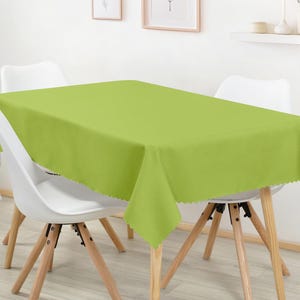 May include: A vibrant lime green tablecloth with a scalloped edge covers a table. White chairs with wooden legs surround the table. The room has a minimalist design. The table is approximately 150 cm long.