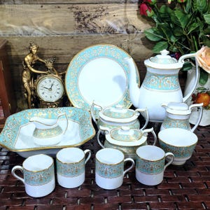 Könnte beinhalten: Ein Porzellan-Teeservice mit weißer Basis und einem verzierten türkisfarbenen und goldenen Blumenmuster. Das Set umfasst eine Teekanne, eine Zuckerdose mit Deckel, ein Milchkännchen, vier Tassen, eine große Servierschale und einen Teller.