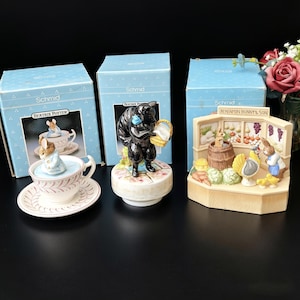 May include: Three Beatrix Potter Schmid ceramic collectibles with original blue boxes. One is a teacup and saucer with a rabbit figurine, one is a black squirrel figurine on a base, and one is a Benjamin Bunny & Son shop scene figurine.
