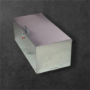 Puede incluir: Una caja de almacenamiento rectangular de metal plateado con tapa con bisagras y asa. La caja tiene un pestillo con una llave roja. La caja está hecha de metal brillante y reflectante.