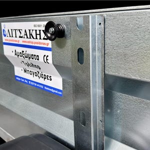 Puede incluir: Primer plano de una plataforma de remolque de metal galvanizado con un rodillo negro y una pegatina con texto griego. La plataforma del remolque tiene una superficie texturizada y un fondo negro.