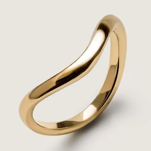 May include: A gold ring with a smooth, curved design. The ring has a flowing, organic shape, with a polished surface that reflects light. The ring is a minimalist piece of jewellery.