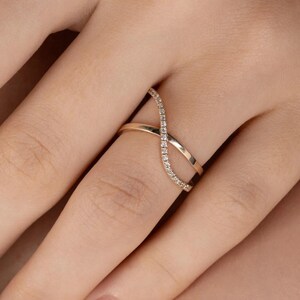 Puede incluir: Un anillo dorado con un dise&ntilde;o de s&iacute;mbolo de infinito. Un lado del s&iacute;mbolo de infinito est&aacute; incrustado con peque&ntilde;as piedras preciosas transparentes. El anillo se lleva en un dedo, mostrando su estilo elegante y moderno. El dise&ntilde;o del anillo es un bucle continuo.