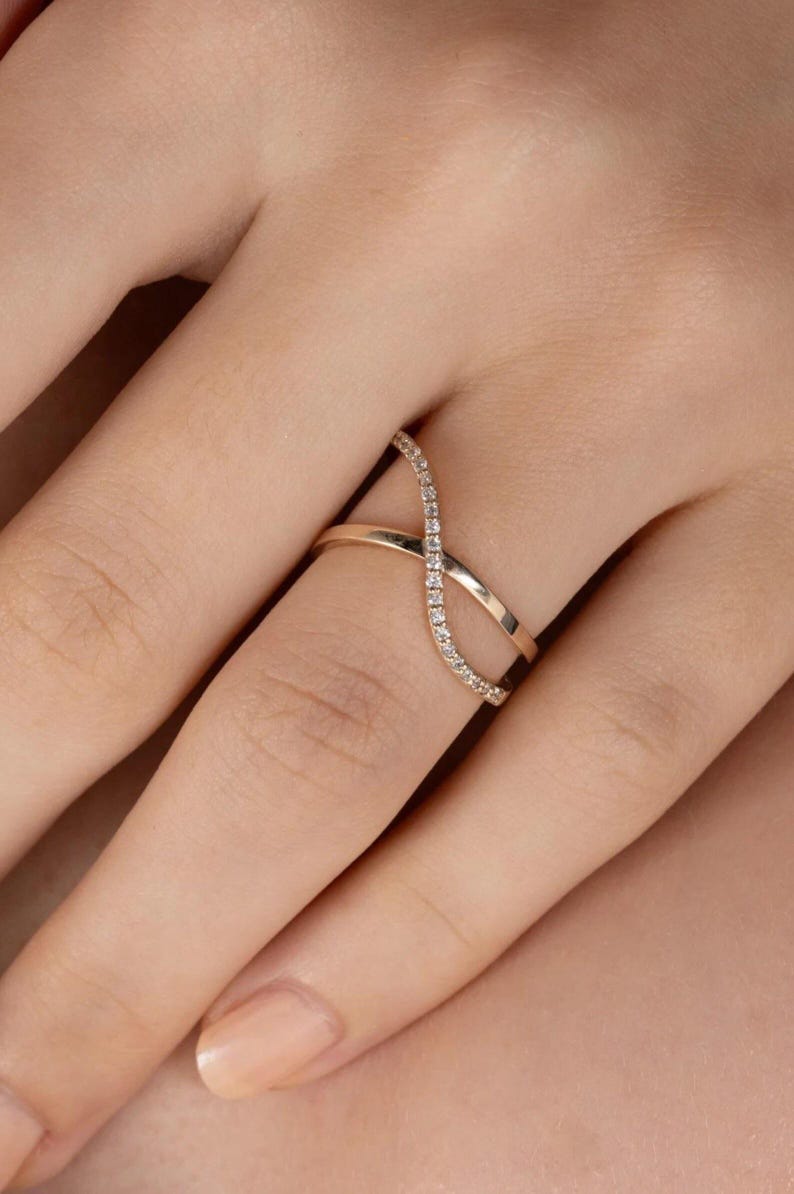 Puede incluir: Un anillo dorado con un dise&ntilde;o de s&iacute;mbolo de infinito. Un lado del s&iacute;mbolo de infinito est&aacute; incrustado con peque&ntilde;as piedras preciosas transparentes. El anillo se lleva en un dedo, mostrando su estilo elegante y moderno. El dise&ntilde;o del anillo es un bucle continuo.