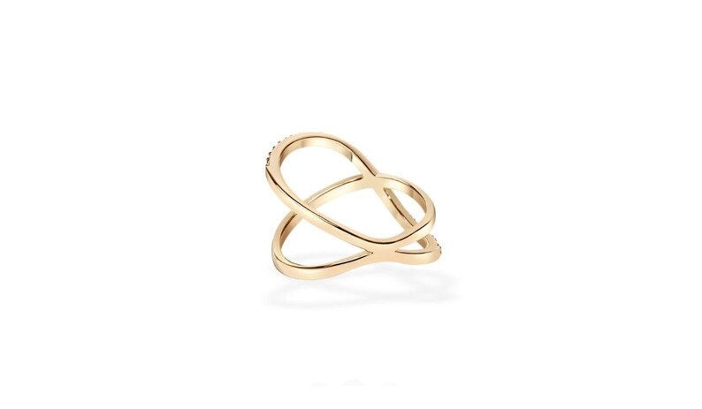 Puede incluir: Un anillo de color dorado con un dise&ntilde;o abierto y superpuesto. El anillo tiene un acabado liso y pulido y algunas piedras peque&ntilde;as y brillantes engastadas en una de las bandas. El anillo est&aacute; sobre un fondo blanco.