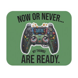 May include: A rectangular mousepad with a sage green background featuring a black game controller illustration with large, teary eyes. The text reads NOW OR NEVER... and MY THUMBS ARE READY. The controller screen displays PLAY ME! ADDICTED?.