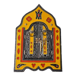 May include: A decorative wall hanging shaped like an arched window with a bright yellow frame, orange accents, and black metal detailing. The central double doors feature intricate silver-toned scrollwork, two circular ring handles, and a brass latch.