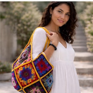 Op de afbeelding: Een kleurrijke, gehaakte tote bag met een patchwork ontwerp. De tas heeft vierkanten in verschillende kleuren, waaronder rood, blauw, paars en geel. De tas heeft gele bandjes en een gele rand rond elke vierkant. De tas wordt over de schouder gedragen.