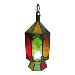 May include: A hanging lantern featuring a hexagonal metal frame with multi-coloured textured glass panels in red, green, yellow, and blue. The structure includes a top suspension loop and a matching hexagonal base, with light emitting from the centre.