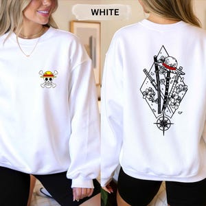 May include: White sweatshirt with a small skull and crossbones graphic on the front and a larger graphic on the back featuring a straw hat, swords, and flowers. The word "WHITE" is above the sweatshirt.