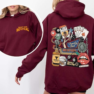 Op de afbeelding: Bordeaux hoodie met de tekst "Treaty Oak Revival" op de voorkant en een afbeelding op de achterkant met speelkaarten, een whiskyfles en lippen. De afbeelding op de achterkant bevat de tekst "Have a nice day" en "No Vacancy".