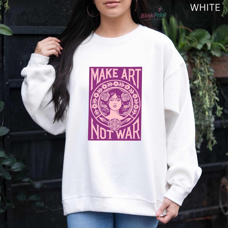 以下が含まれることがあります： 「MAKE ART NOT WAR」と書かれた紫色のグラフィックが特徴の白いスウェットシャツ。 グラフィックは、花の要素に囲まれた女性の顔を特徴としています。 スウェットシャツは長袖とクルーネックです。