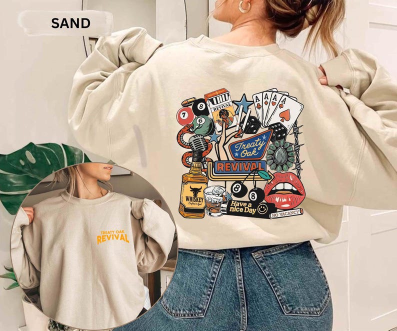 Op de afbeelding: Zandkleurige sweatshirt met een afbeelding op de achterkant met een fles whisky, speelkaarten, dobbelstenen en de woorden "Treaty Oak Revival". De voorkant van de sweatshirt heeft de woorden "Treaty Oak Revival" in oranje.