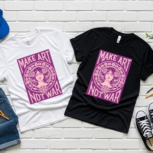 以下が含まれることがあります： 白と黒の2枚のTシャツ。紫色のグラフィックで「MAKE ART NOT WAR」と書かれています。女性の顔と花の要素が描かれています。青い野球帽、ジーンズ、スニーカーも写っています。