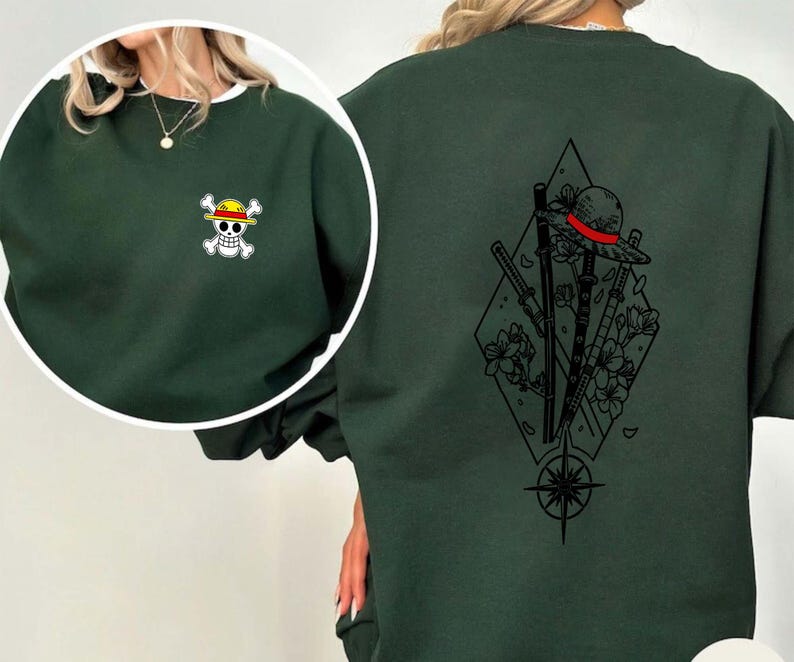 May include: Dark green sweatshirt with a white-trimmed neckline. The front features a small embroidered pirate skull and crossbones. The back displays a black graphic of a hat, swords, flowers, and a compass rose within a diamond.