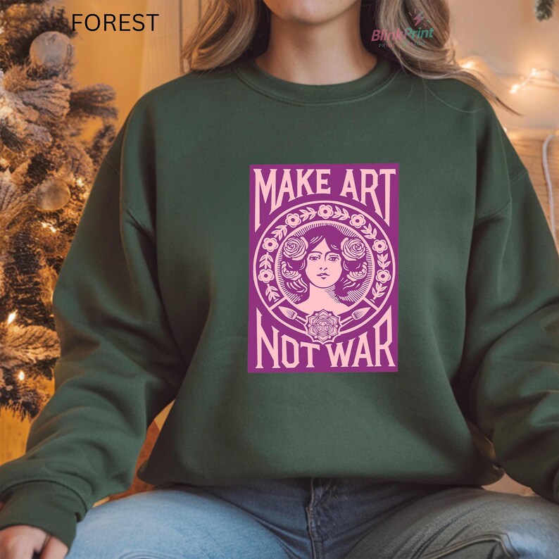 以下が含まれることがあります： 「MAKE ART NOT WAR」と書かれた紫色のグラフィックが特徴のフォレストグリーンのスウェットシャツ。 グラフィックには、花の要素に囲まれた女性の顔が含まれています。 「FOREST」という単語が左上隅に白で印刷されています。