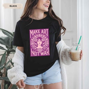 以下が含まれることがあります： 「MAKE ART NOT WAR」と書かれた紫とピンクのグラフィックが特徴の黒いTシャツ。グラフィックは、花の要素に囲まれた女性の顔が特徴です。このシャツは、青いデニムショーツと組み合わせています。