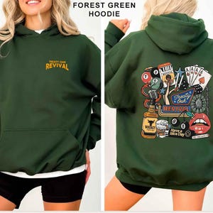 Op de afbeelding: Bosse groene hoodie met de tekst "Treaty Oak Revival" op de voorkant en een afbeelding op de achterkant. De afbeelding op de achterkant bevat een whiskyfles, speelkaarten en lippen.