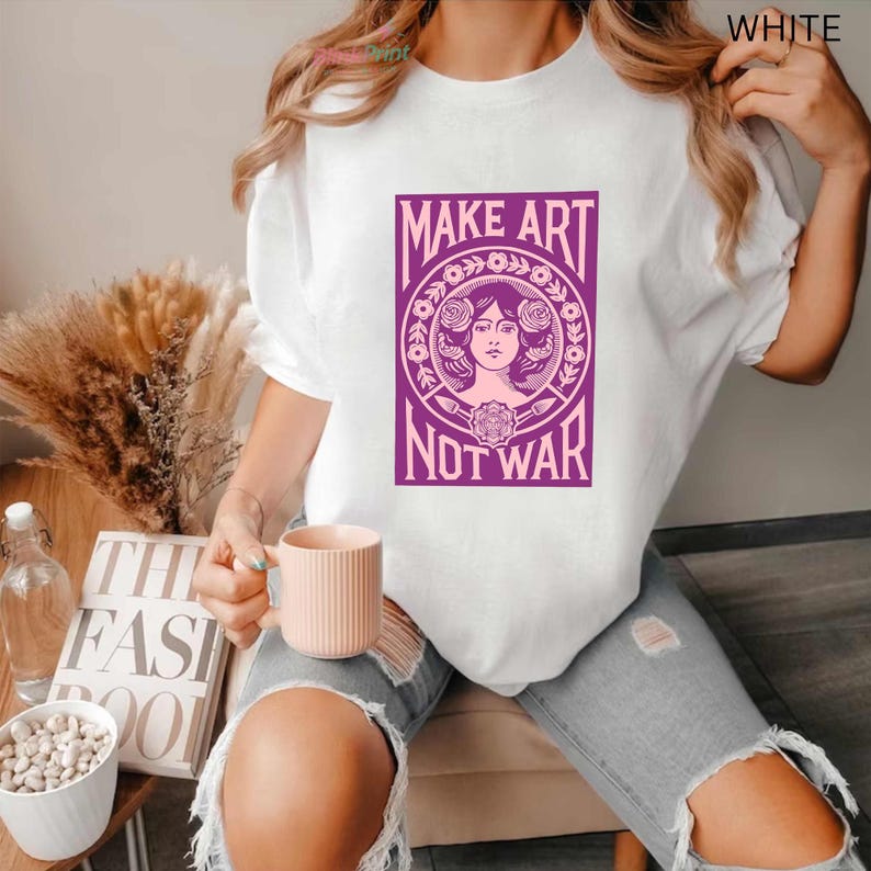 以下が含まれることがあります： 「MAKE ART NOT WAR」と書かれた紫色のグラフィックが特徴の白いTシャツ。グラフィックは、花の要素に囲まれた女性の顔が特徴です。このシャツはカジュアルなスタイルで、普段使いに適しています。
