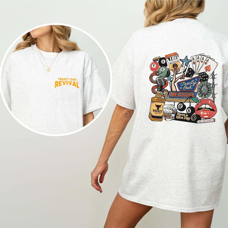 Op de afbeelding: Lichtgrijs t-shirt met de tekst "Treaty Oak Revival" in oranje op de voorkant en een kleurrijke afbeelding op de achterkant. De afbeelding bevat een whiskyfles, speelkaarten, dobbelstenen en een paar rode lippen.