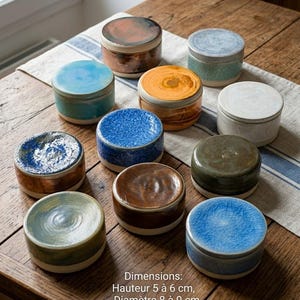 Op de afbeelding: Een verzameling keramische potten met deksels in verschillende kleuren, waaronder blauw, oranje, bruin en groen. De potten zijn rond en staan op een houten tafel. De afmetingen zijn 5 tot 6 cm hoog en 8 tot 9 cm in diameter.