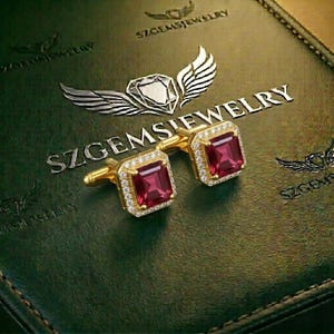 Könnte beinhalten: Goldene Manschettenknöpfe mit quadratischen, roten Edelsteinen und einem Kranz aus kleinen, klaren Steinen. Die Manschettenknöpfe werden auf einer dunkelgrünen Oberfläche mit dem geprägten Text "SZGEMSJEWELRY" und einem Diamant- und Flügel-Logo präsentiert.