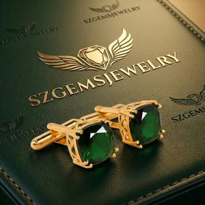 May include: Gold-toned cufflinks with large, square emerald-green gemstones. The cufflinks are set on a dark green leather-like surface with the text "SZGEMSJEWELRY" in gold lettering and a gold emblem.