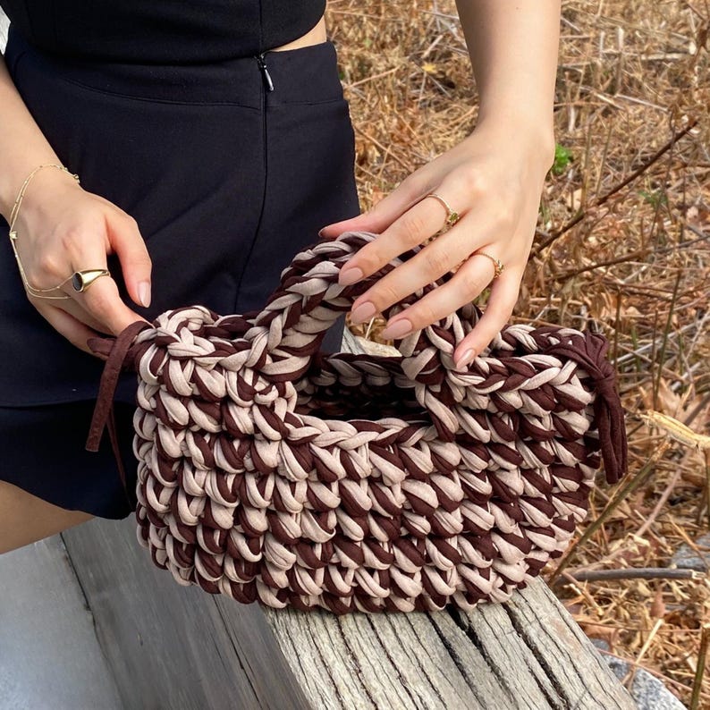 Puede incluir: Bolso tote tejido a mano en marr&oacute;n y beige. El bolso presenta un dise&ntilde;o tejido resistente, forma redondeada y asa. El bolso est&aacute; hecho de un material suave y texturizado, con un estilo informal.