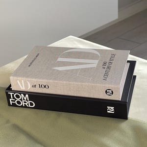 Op de afbeelding: Twee hardcover boeken op elkaar gestapeld. Het bovenste boek is lichtbeige met de tekst "AD at 100 A Century of Style". Het onderste boek is zwart met de tekst "TOM FORD". De boeken liggen op een lichtgroen oppervlak.
