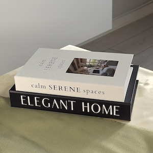 Puede incluir: Libros decorativos apilados con los títulos "calm SERENE spaces" y "ELEGANT HOME". El libro superior es blanco con una pequeña imagen y texto negro. El libro inferior es negro con texto blanco. Los libros están sobre una superficie verde claro.