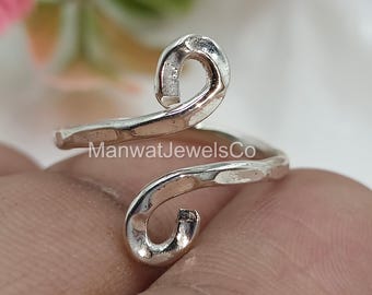 May include: A silver-colored ring with a hammered texture and a unique, swirling design. The ring features the text "ManwatJewelsCo". The ring's design includes two curved ends that create a stylish and eye-catching look.