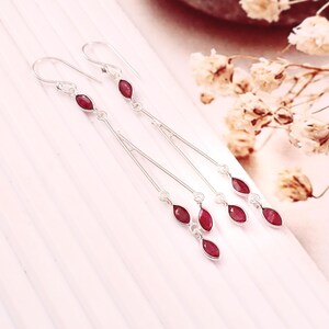 May include: A pair of long silver drop earrings featuring multiple marquise-cut deep red gemstones. Each earring consists of a thin silver wire structure with stones set at intervals, suspended from a simple silver hook for pierced ears.
