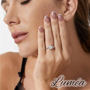 May include: A silver ring featuring a central, round, clear gemstone. The ring has a twisted band design. The word "Lumea" is written in cursive script in the lower right corner of the image.