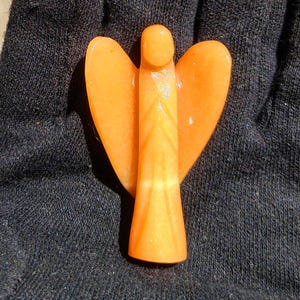 Puede incluir: Figurita de ángel naranja de piedra, con alas extendidas. El diseño es simple y elegante. La piedra tiene una calidad translúcida, con sutiles variaciones de color. Un objeto decorativo.